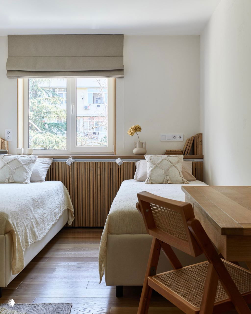 Светлая комната с двумя кроватями и узким деревянным подоконником, оформленным в натуральных тонах и с деревянной решёткой радиатора под окном.