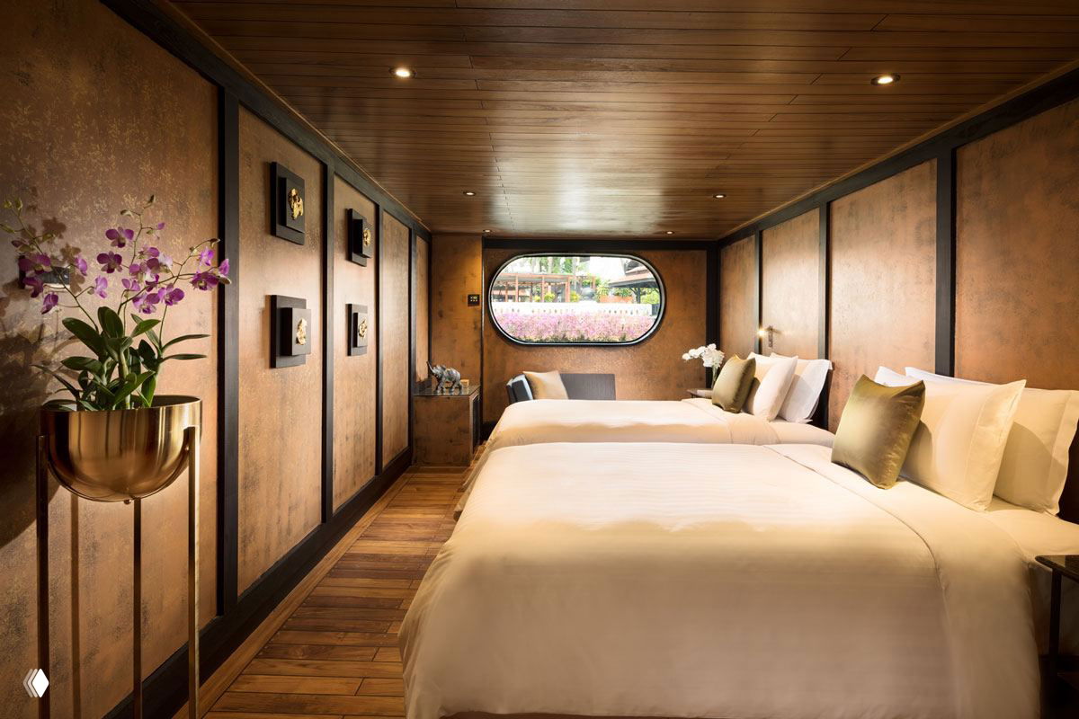 Каюта с двумя кроватями и деревянным полом, оформленная в природных оттенках с мягкими подушками и иллюминатором, открывающим вид на причал.