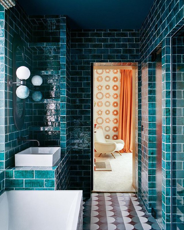 Уютный уголок с большим круглым окном и скамьёй в полосатой ткани, на столе ваза с ярким букетом; естественный свет подчёркивает текстуры и цвета интерьера.