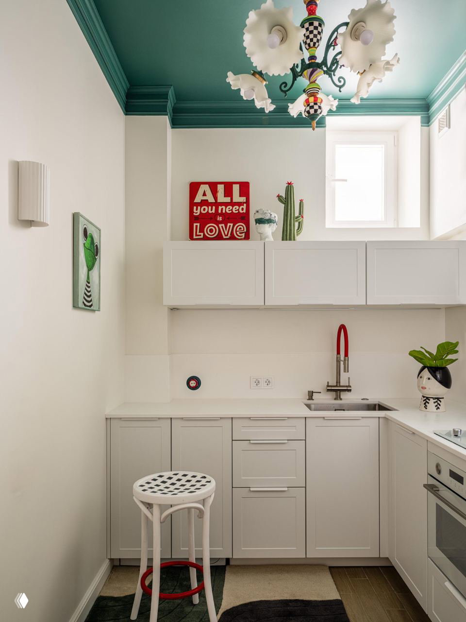 Небольшая кухня с бирюзовым потолком и декоративной люстрой, белые шкафы, плакат «ALL you need is LOVE» и яркие аксессуары.