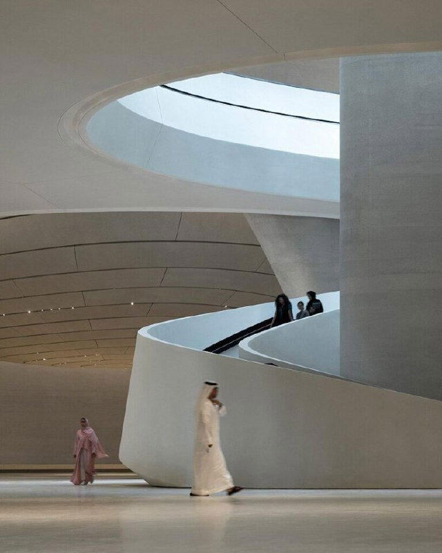 Панорамный вид галереи музея с спиралевидными элементами и гладкими поверхностями пола и стен; простор для экспозиций и движение посетителей в светлом пространстве.