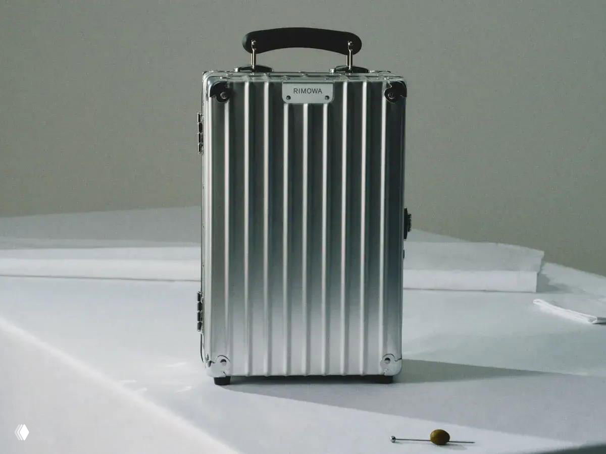 Фронтальный вид алюминиевого рифленого кейса Rimowa с кожаной ручкой и фирменной табличкой, стилизованный для презентации коллаборации с Robbe & Berking.