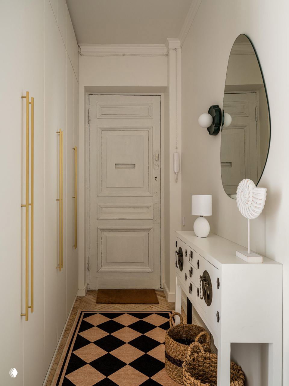 Прихожая сталинской квартиры: старинная входная дверь, белый консольный стол с декоративными элементами, круглое зеркало и плетёные корзины.