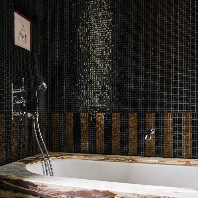 Ванная с тёмной мозаичной плиткой на стенах, бортик ванны с деревянной вставкой и хромированный смеситель — интерьерная фотосъёмка акцентов отделки