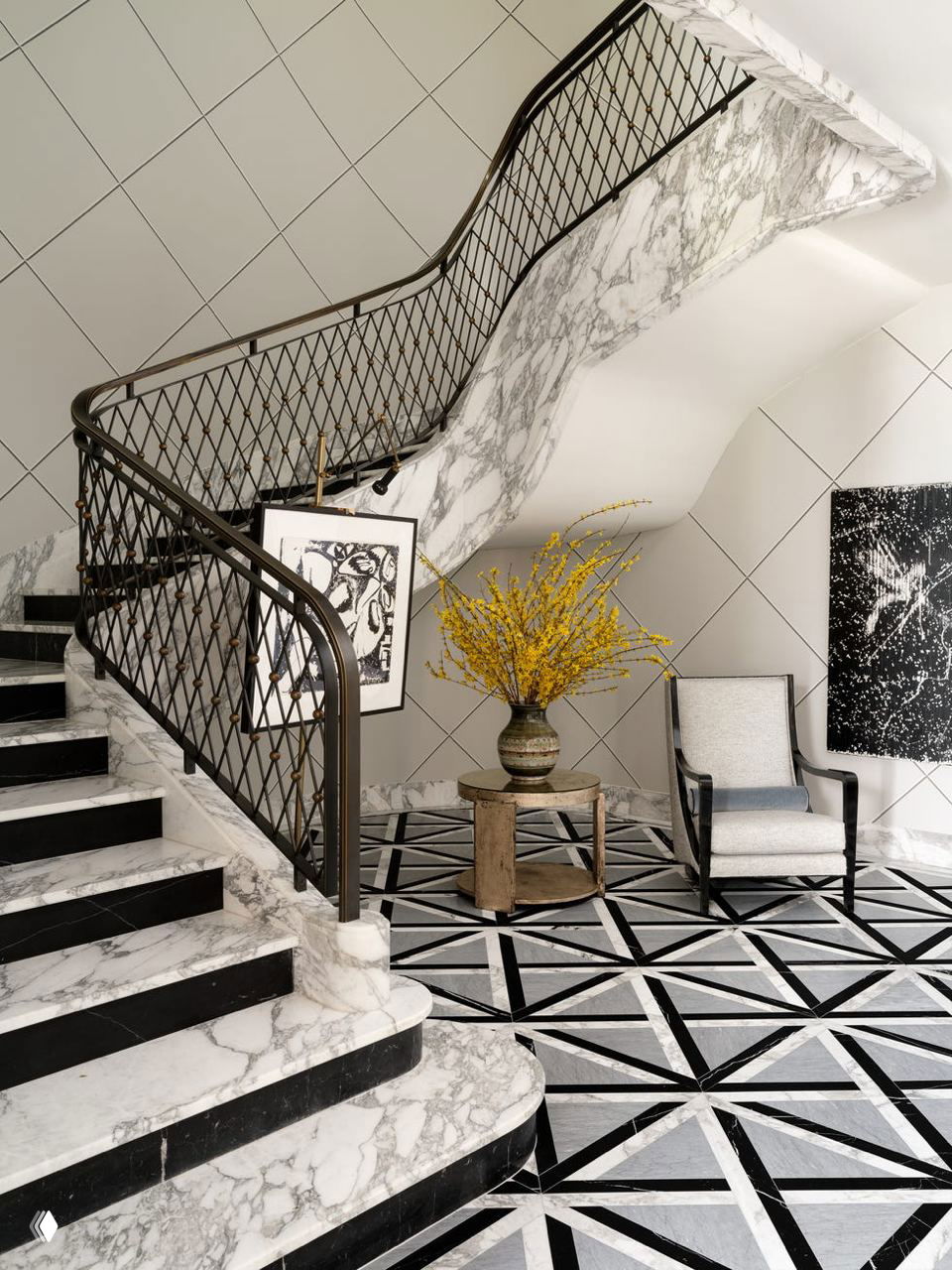 Парадная мраморная лестница с металлическими перилами; у входа геометрический черно‑белый пол и вазон с желтыми ветками.