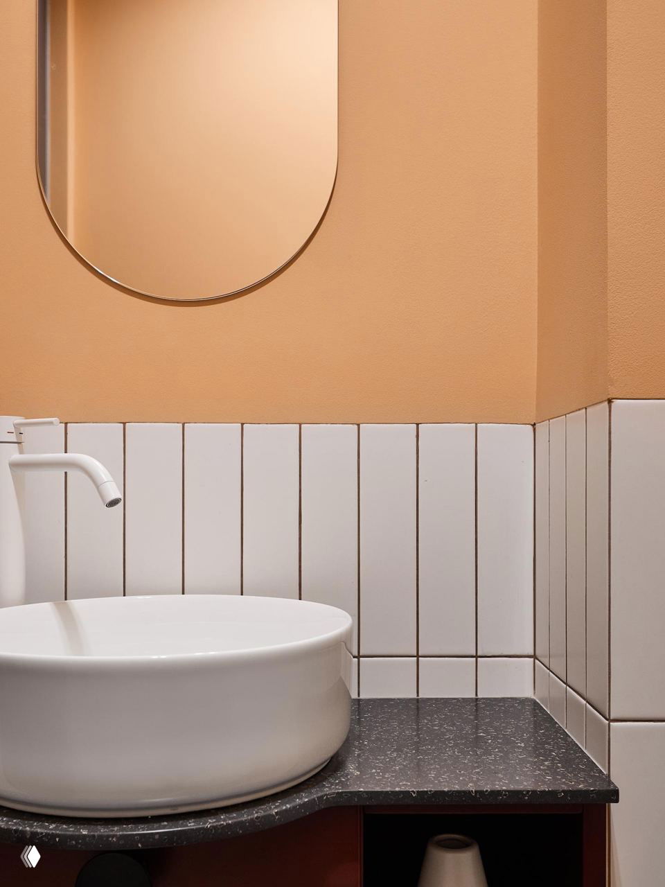 Крупный план раковины и фрагмента стены, окрашенной в мягкий персиково-терракотовый тон, белая круглая раковина на тёмной столешнице.