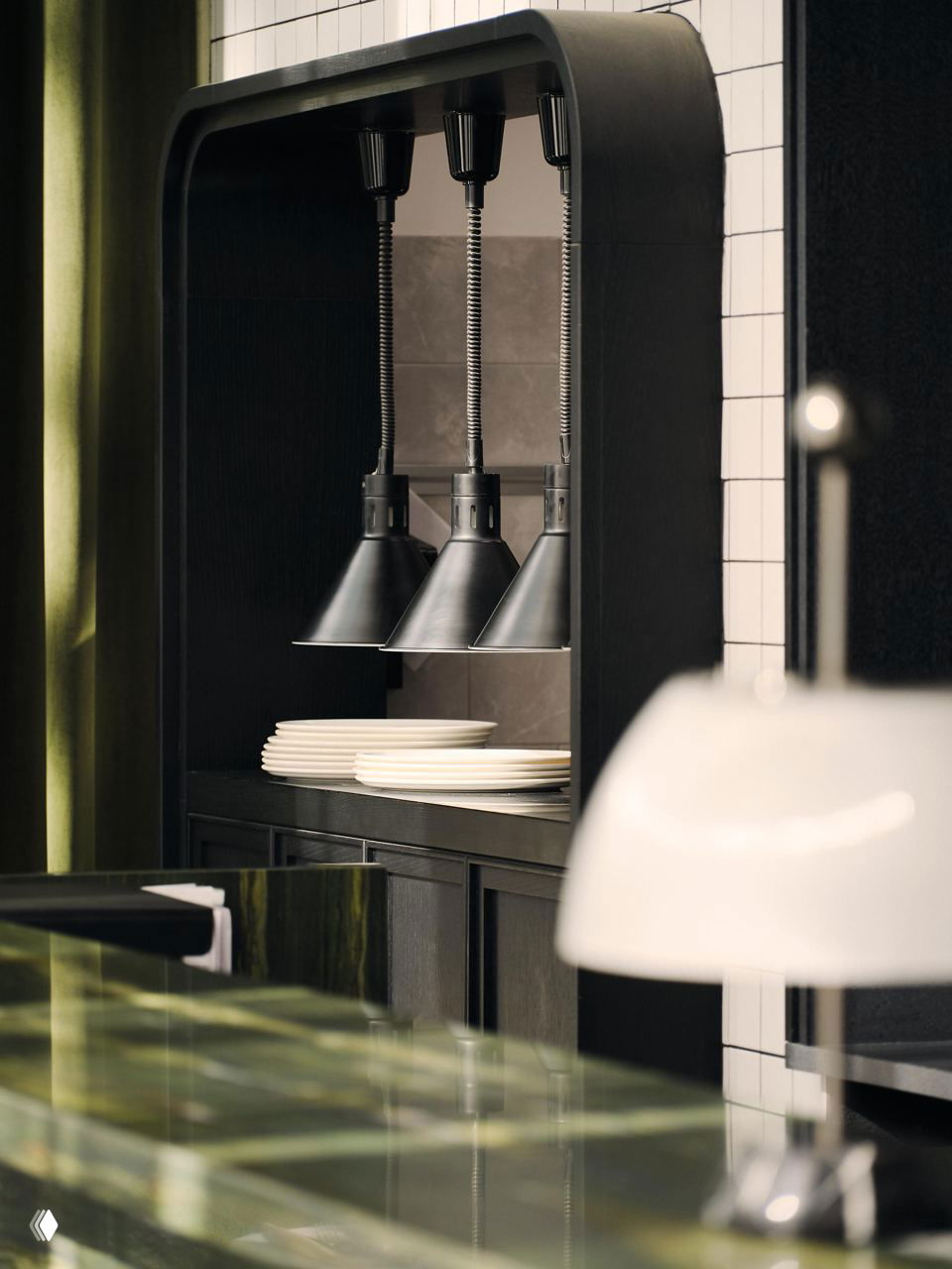 Фрагмент сервировочной части кухни с подвесными лампами над проходом и аккуратно сложенными тарелками, часть служебной зоны ресторана.