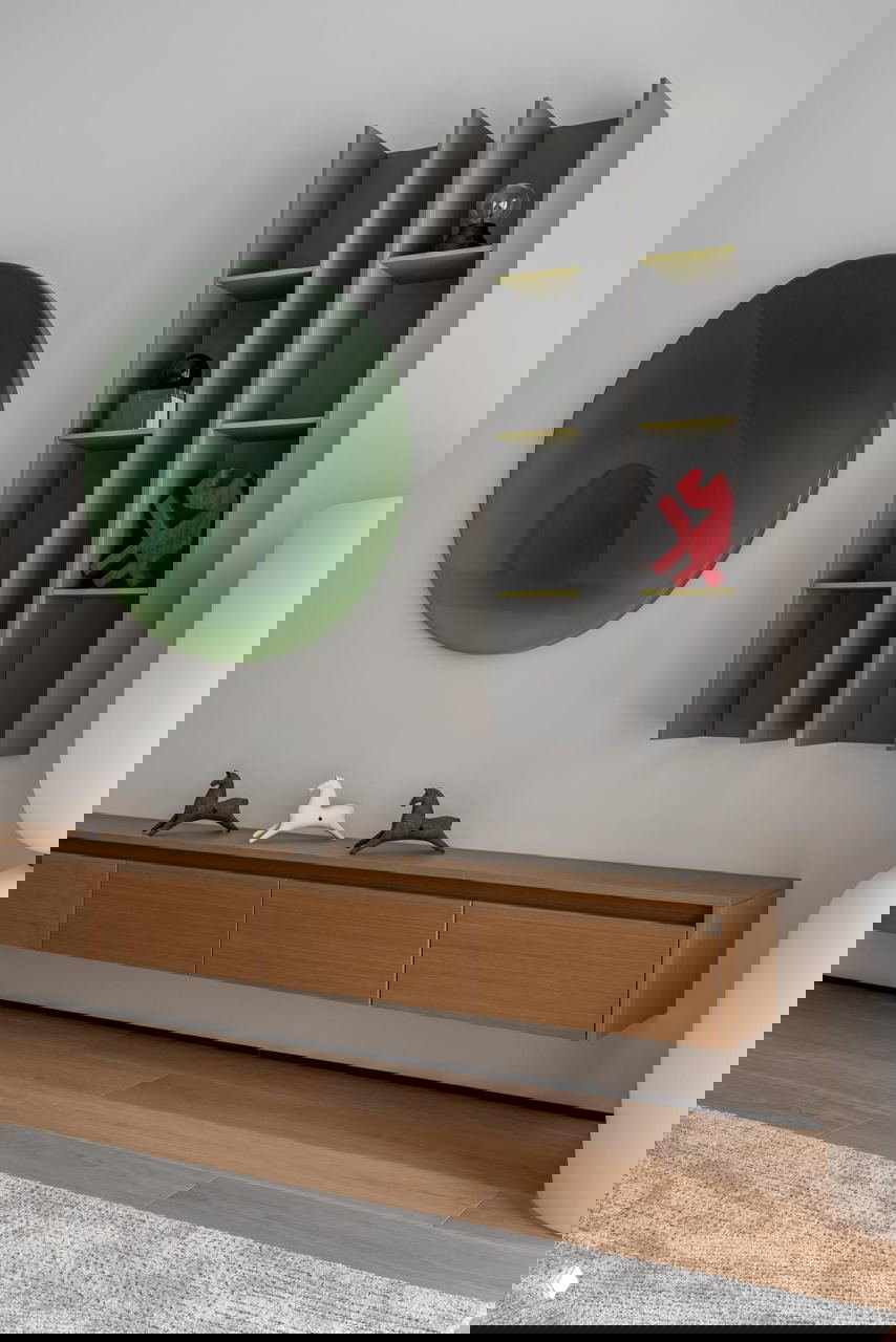 Настенная инсталляция и плавающая деревянная тумба в гостиной: зелёная круглая арт-панель и вертикальные полки с декоративными предметами на нейтральном фоне.