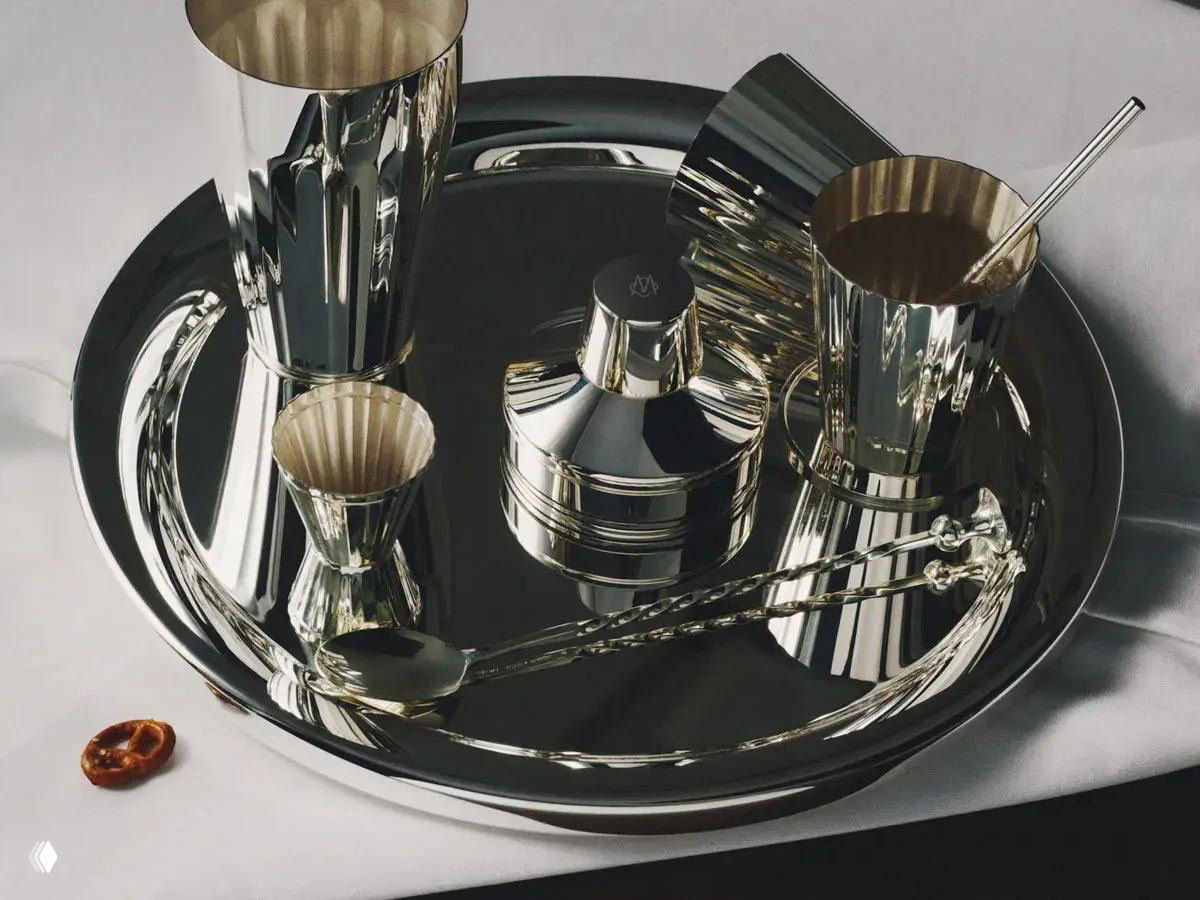 Сервировочная композиция на подносе: посеребренные стаканы, шейкер и соломинки отражаются в гладкой поверхности подноса Robbe & Berking.