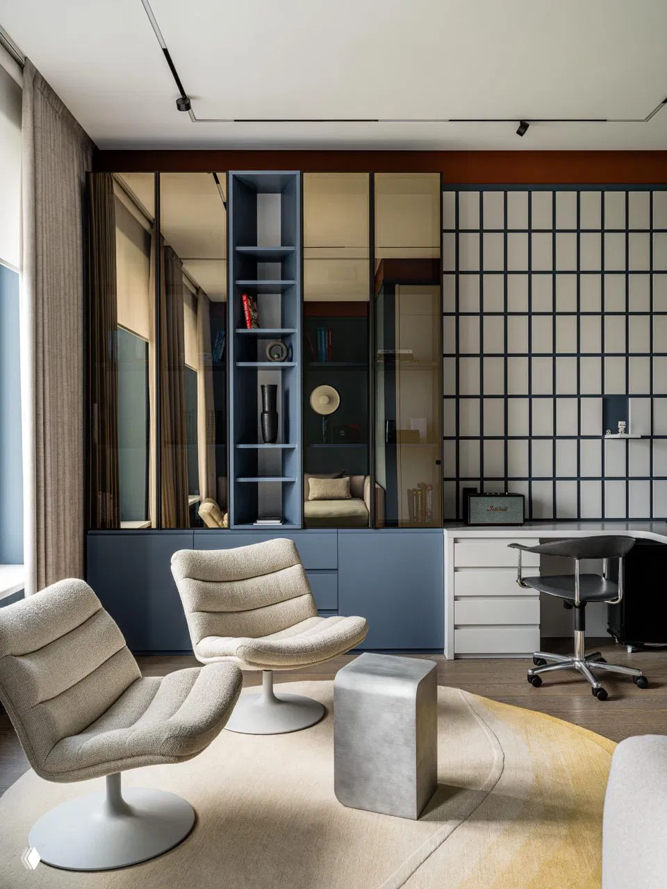 Рабочая зона/кабинет с модульными шкафами в сине‑серой гамме, мягкими креслами и декоративной решётчатой облицовкой на стене.
