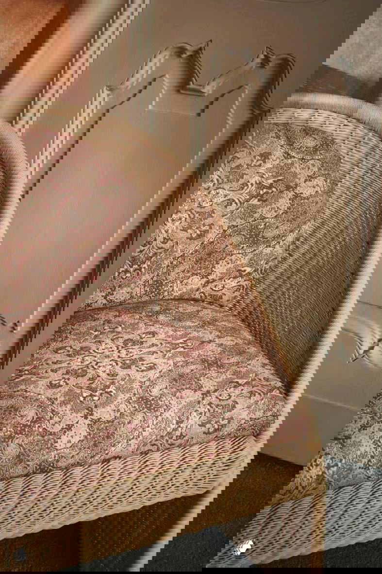 Плетёное кресло с мягкой сидушкой в орнаментальном узоре на фоне декоративной панельной отделки и тёплой палитры.