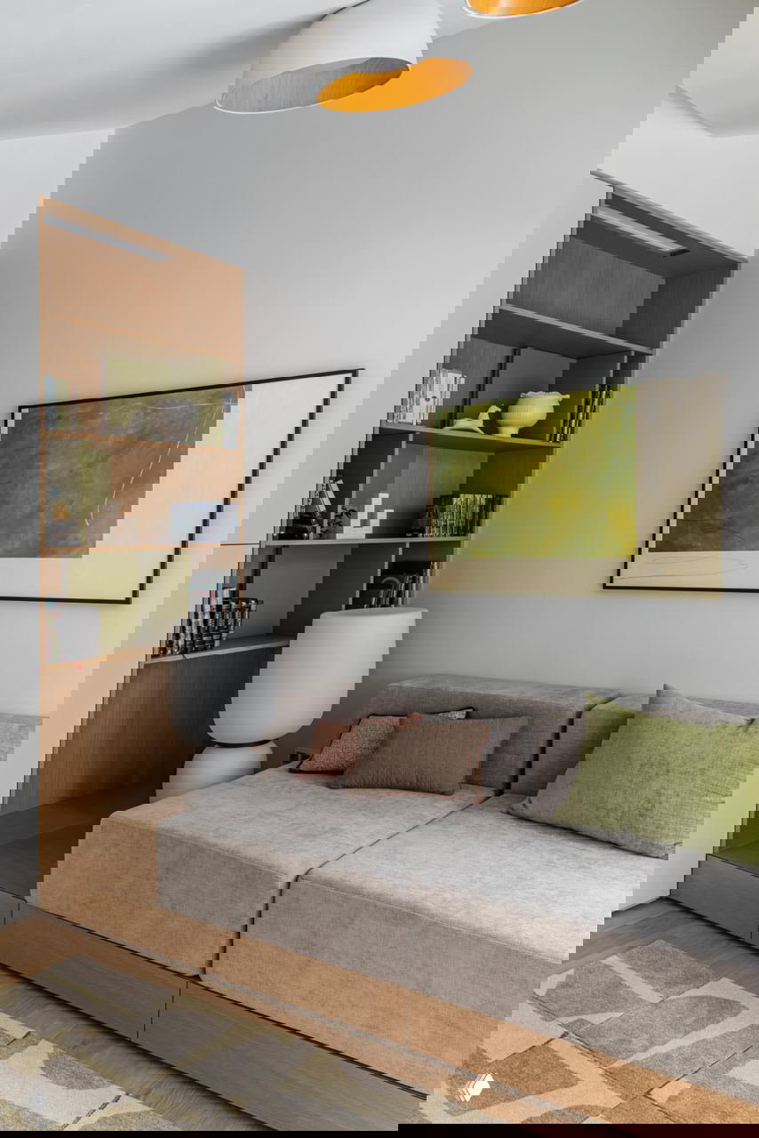 Уютная угловая зона с модульным серым диваном, открытыми полками с книгами и декоративными элементами; пастельные и природные оттенки в оформлении.