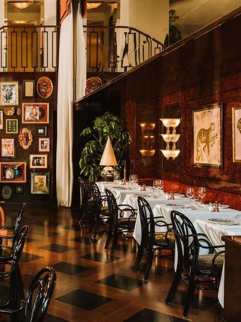 Обеденная зона Gloria Ostería: длинные сервированные столы у стены, картины в рамках, высокие шторы и тёплый деревянный паркет.