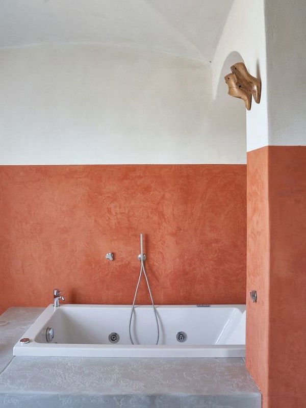 Ванная с белой встроенной ванной и стеной, покрытой фактурной терракотовой штукатуркой до половины высоты комнаты, минимализм в деталях.