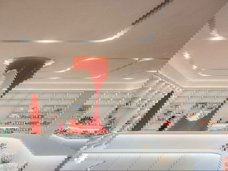 Яркий интерьер второго зала: белые поверхности и крупная оранжево‑красная скульптурная деталь, органично вписанная в книжное пространство и кафейную зону.