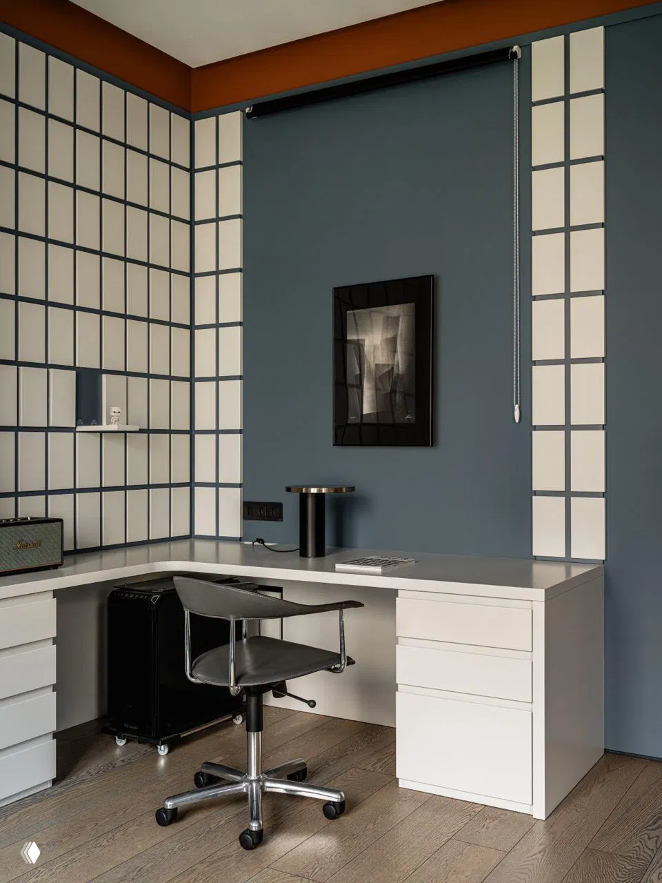 Рабочее место с белым столом в углу, стул на колёсах и решётчатая графическая отделка стен в сочетании с тёплым коричневым карнизом.