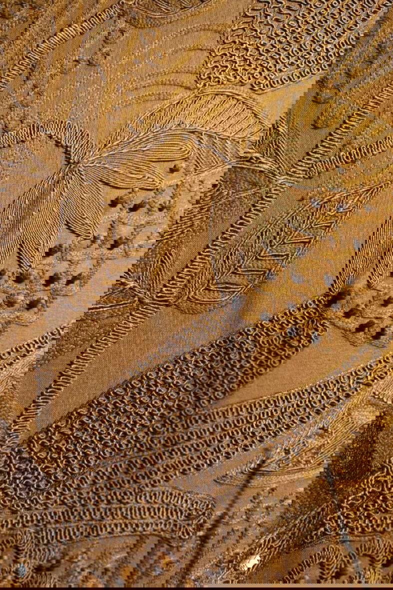 Крупный план декоративной вышивки и фактурных швов на ткани золотисто-горчичных тонов с растительными мотивами.