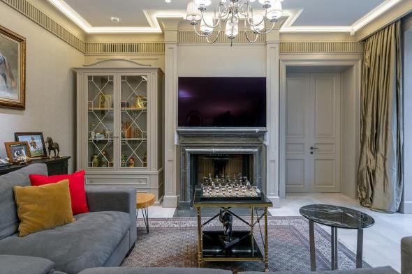 Гостиная с камином в стиле современной американской классики: диван, журнальный столик, высокий потолок и декоративные элементы в интерьере.