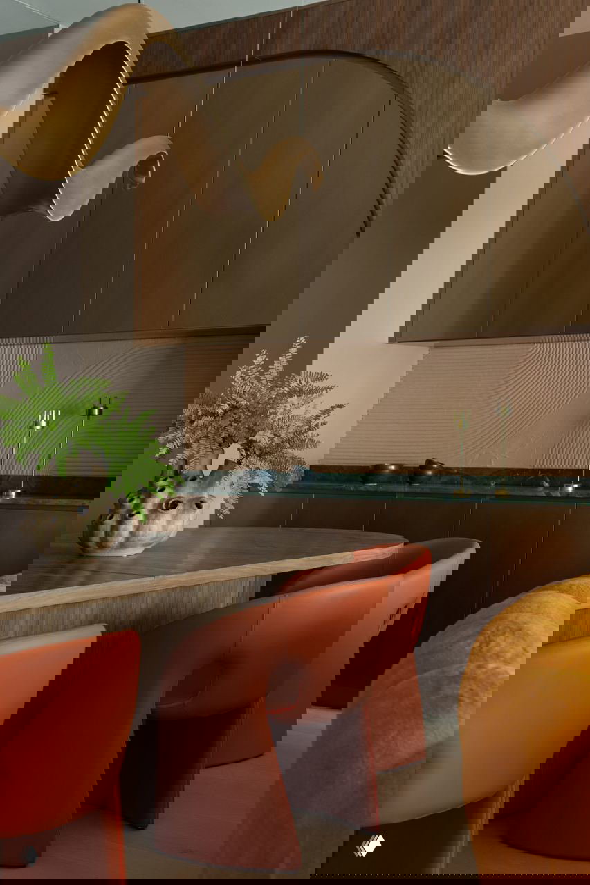 Обеденная зона в пентхаусе: деревянный стол, мандариновые кожаные стулья, оливковые фасады и волнообразная подвесная декоративная скульптура над столом.