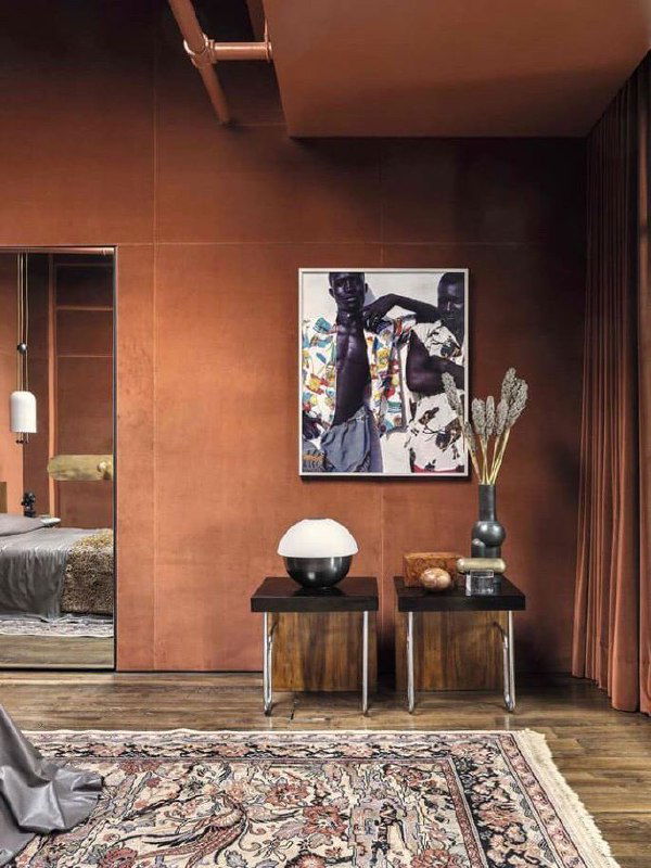 Уютная комната с бархатными шторами и тёмно-терракотовыми стенами, декоративная картина и низкие столики на деревянном полу создают атмосферу.