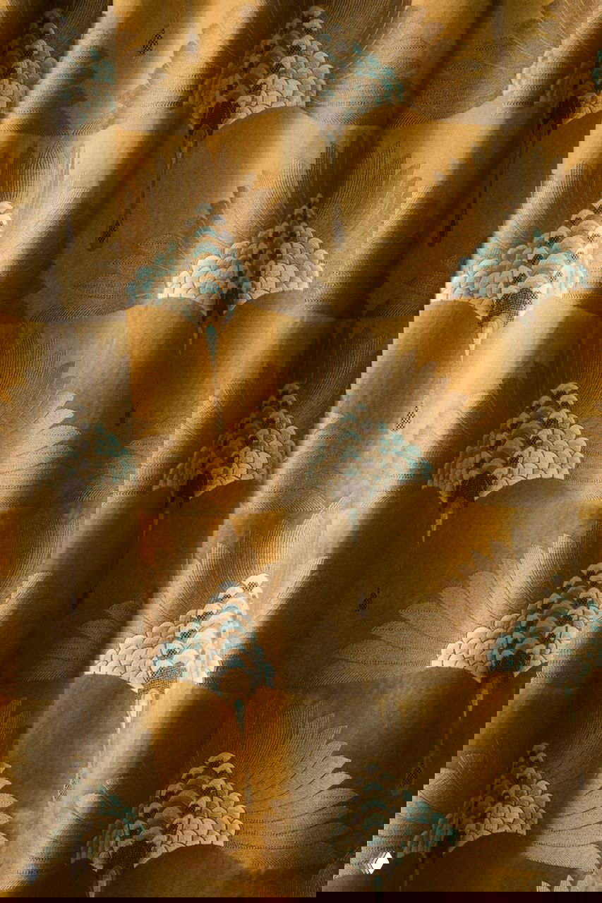 Драпировка с крупным повторяющимся декоративным мотивом в охристых и бирюзовых тонах, мягкая ткань собрана в складки.