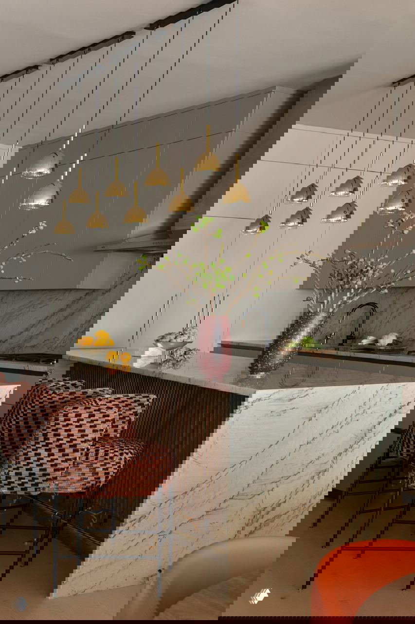 Кухня с островом из белого мрамора, зелёной столешницей, золотыми подвесными светильниками и барными стульями с геометрическим узором — элегантная зона приготовления.