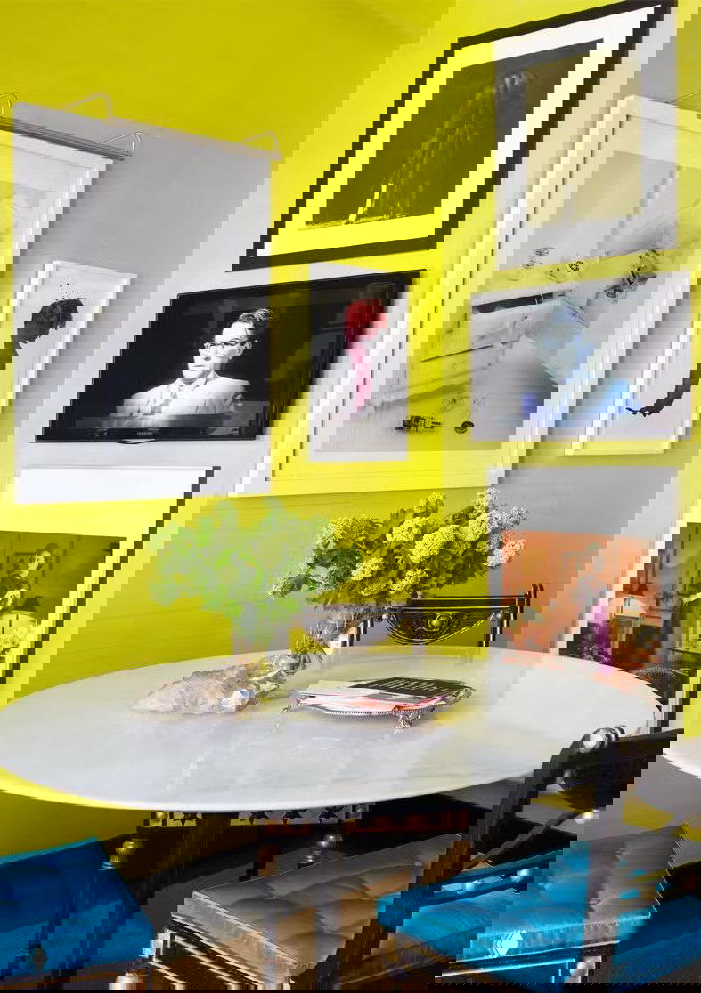 Яркий интерьер со стеной насыщенного лаймово‑зелёного цвета, белый стол и синие стулья создают контрастную палитру для столовой зоны.