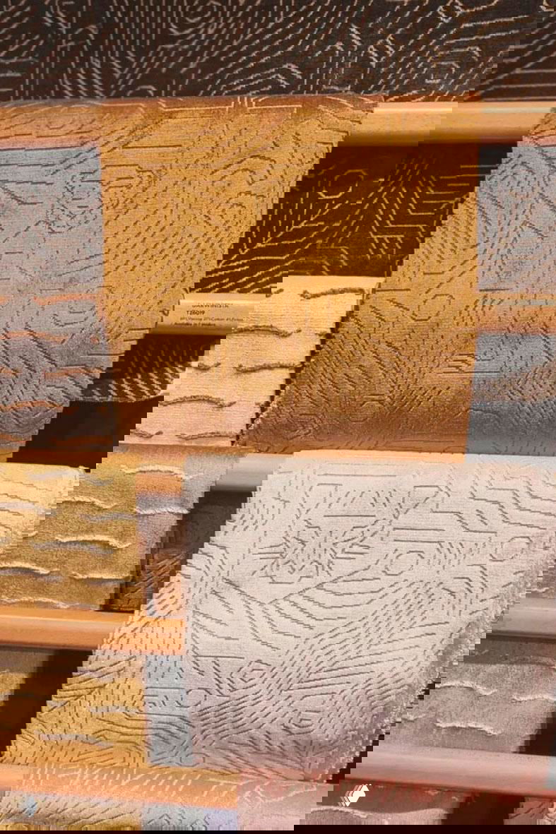 Рулоны тканей и образцы с графическими и звериными мотивами, золотистые и пастельные оттенки на деревянных планках.