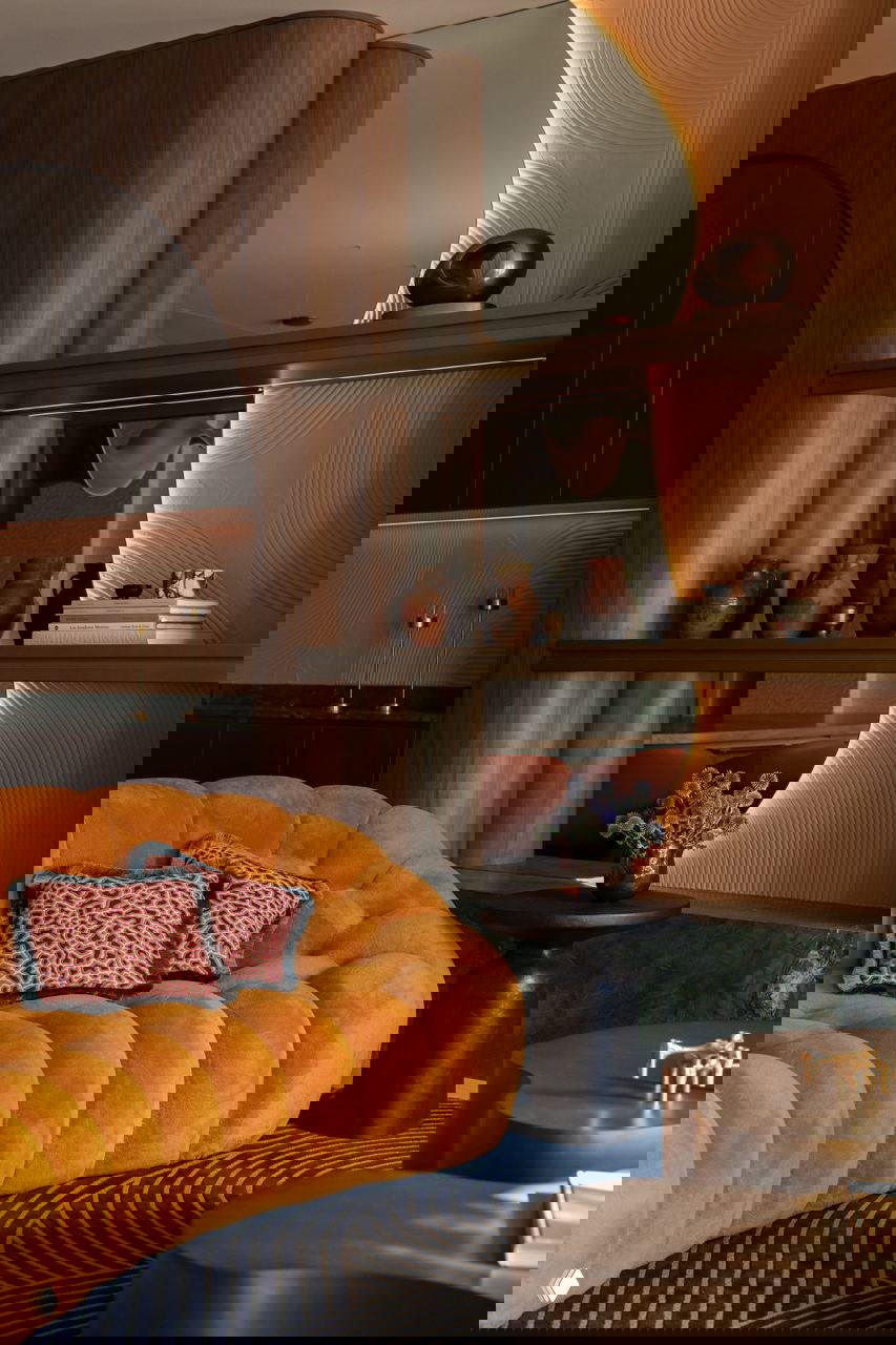 Уютный угол с бархатным охристым диваном, деревянными полками, декоративными керамическими вазами и тёплой подсветкой — богатая палитра материалов.