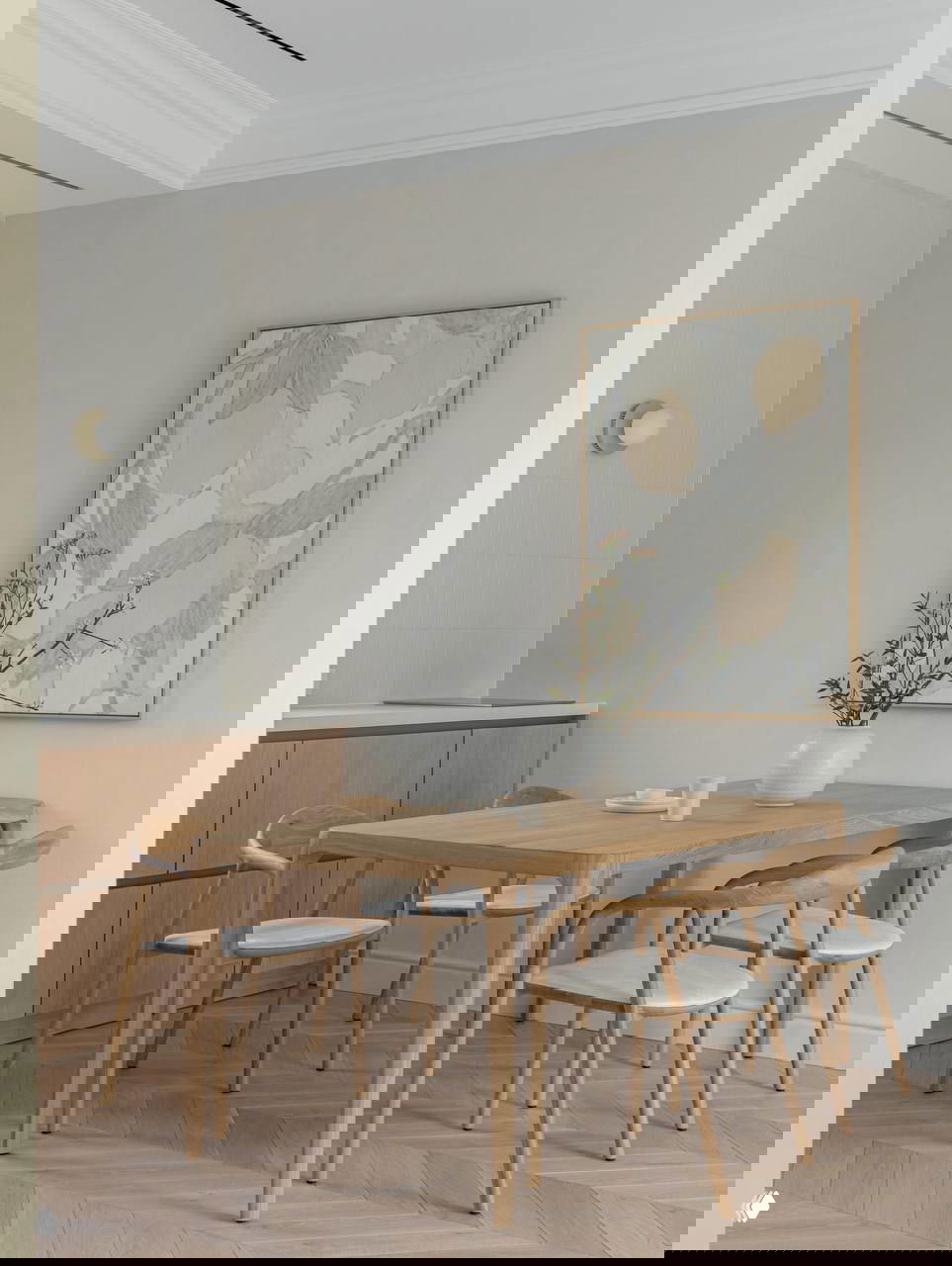 Обеденная группа: светлый деревянный стол и стулья скандинавского стиля, на стене крупная картина и ваза с веткой — натуральный акцент в интерьере.