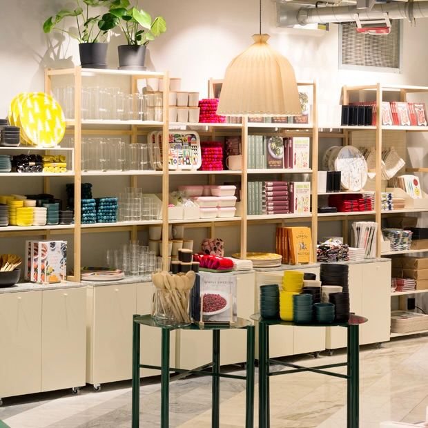 Ряд открытых стеллажей с аккуратно расставленной посудой, светильниками и декоративными предметами в нейтральной палитре — витрина современного интерьерного магазина.