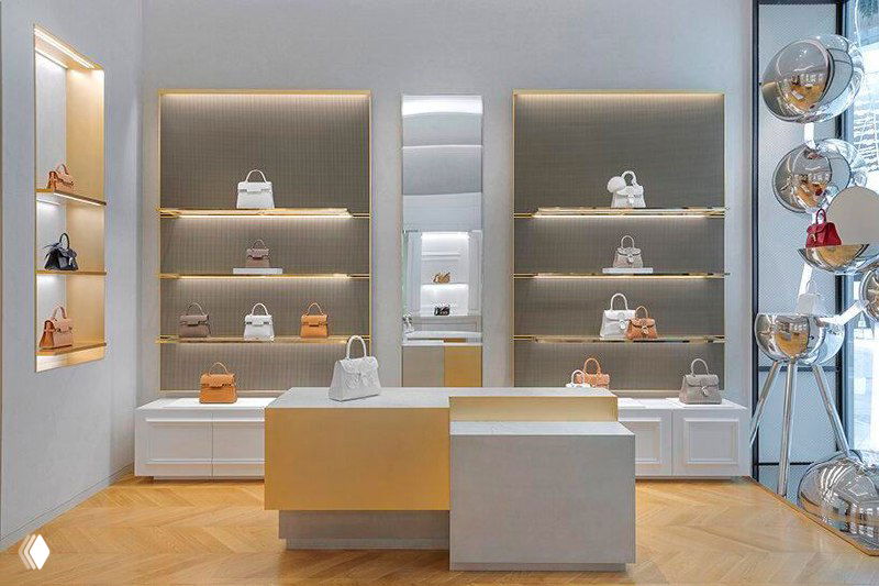 Ряды витрин с подсветкой и выставленными сумками Delvaux: архитектурные ниши, аккуратные подиумы и чистая нейтральная палитра отделки.