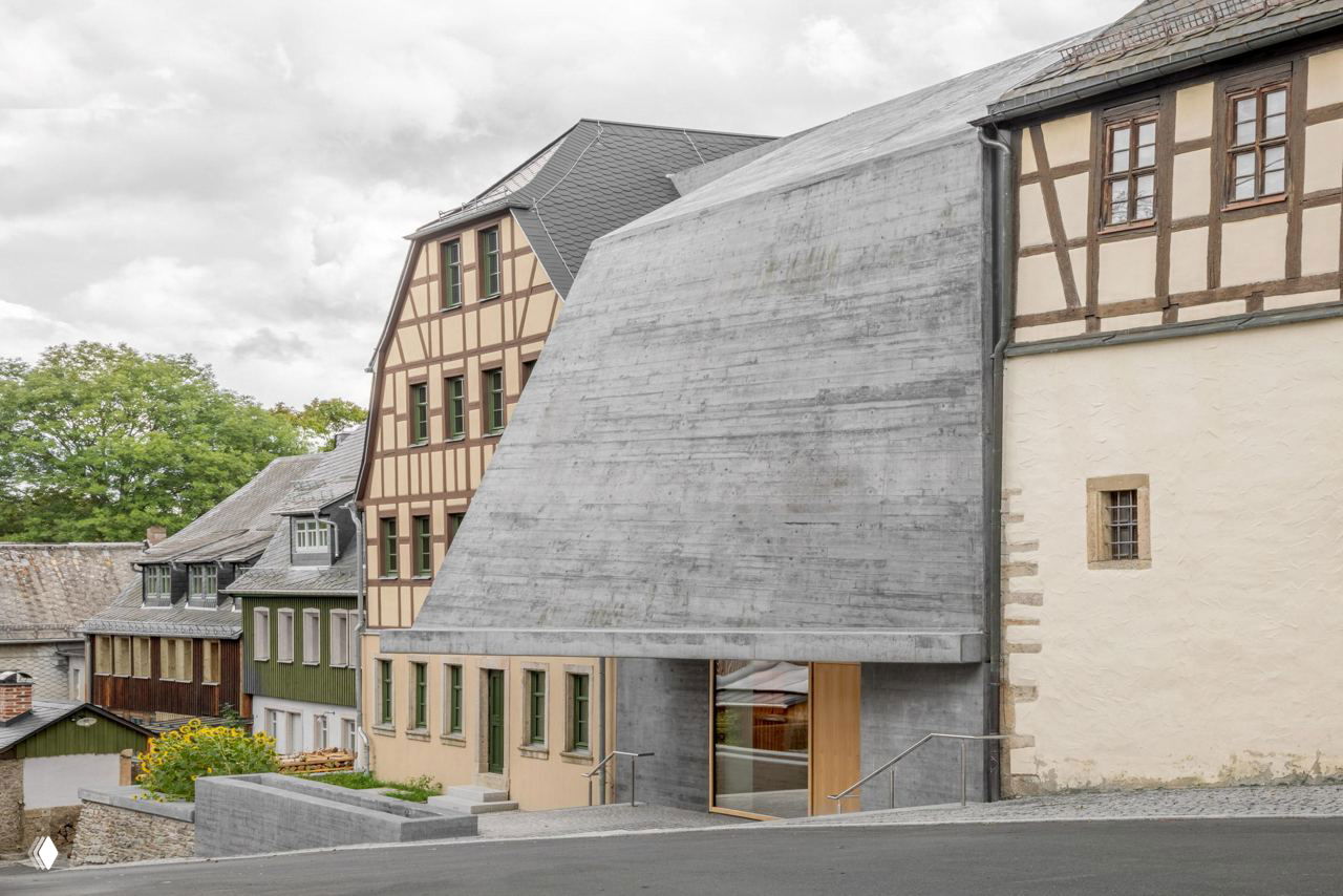 Общий вид: грубая бетонная форма музея сочетается с традиционной тканью фахверковых домов — контраст материалов и масштабов в уличной перспективе