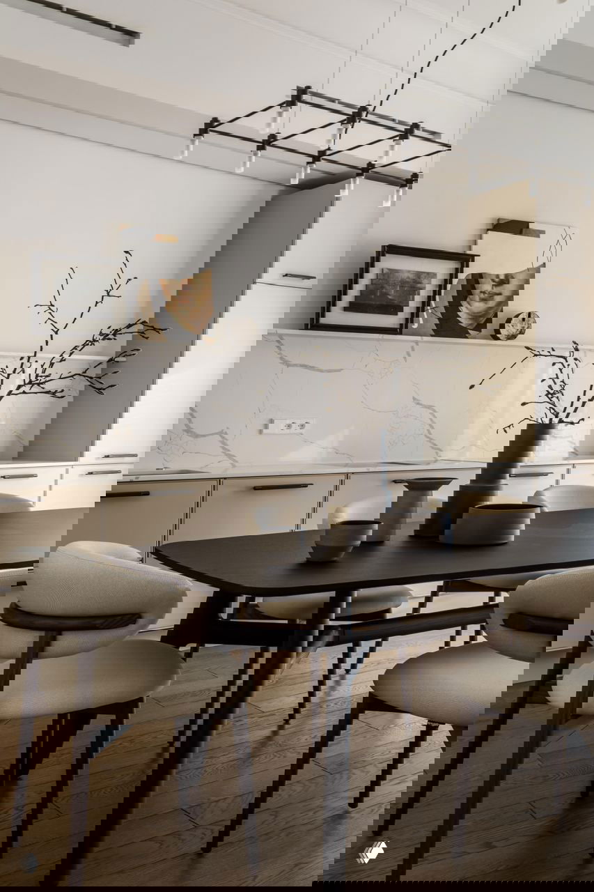 Столовая и кухня в спокойной палитре: тёмный деревянный стол, минималистичные стулья и фактурный фартук, композиция из керамики и ветки.