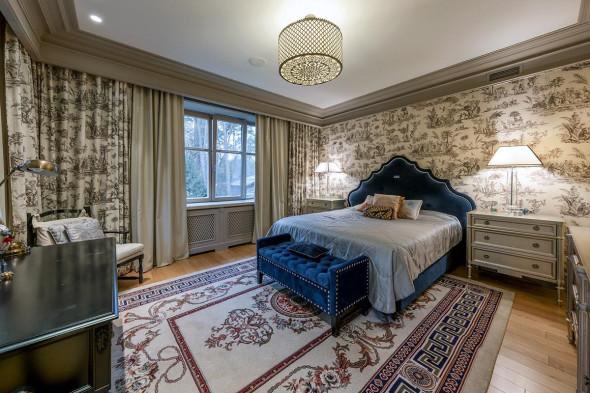 Ещё одна спальня с синим изголовьем и узорными обоями, прикроватными тумбочками и мягким ковром — более уютный интерьер для гостей или жильцов.