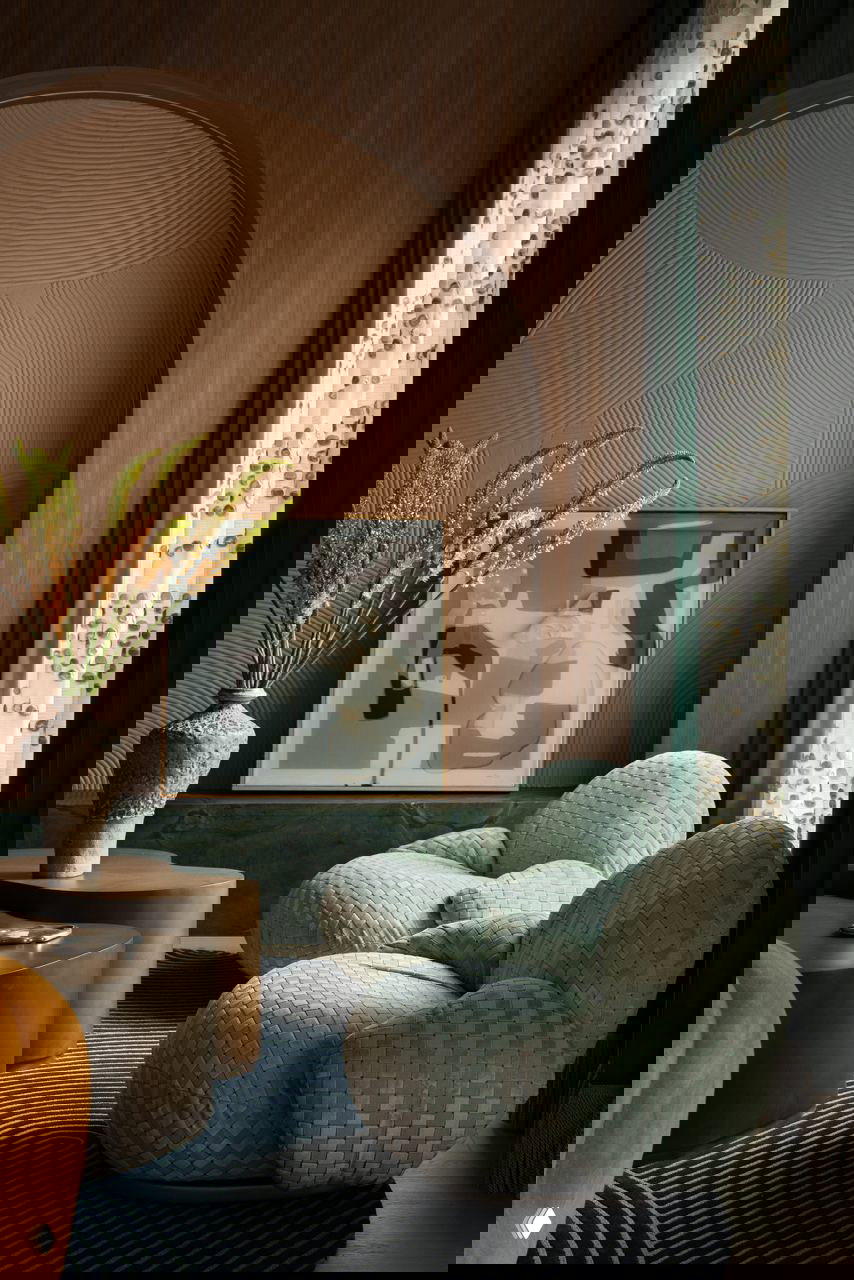 Зона отдыха с плетёными салатовыми креслами перед арочной деревянной нишей и текстурной стеной; глубокие зелёные шторы подчёркивают композицию и фактуры.