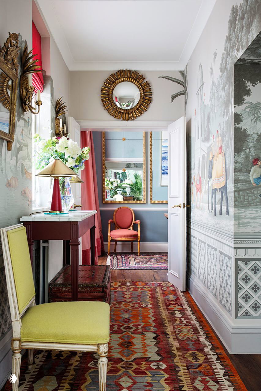 Холл с пастельными панорамными обоями de Gournay, украшенными изображениями индийских слонов; видно зеркало в золотой раме, консольный стол и восточный ковер вдоль прохода.