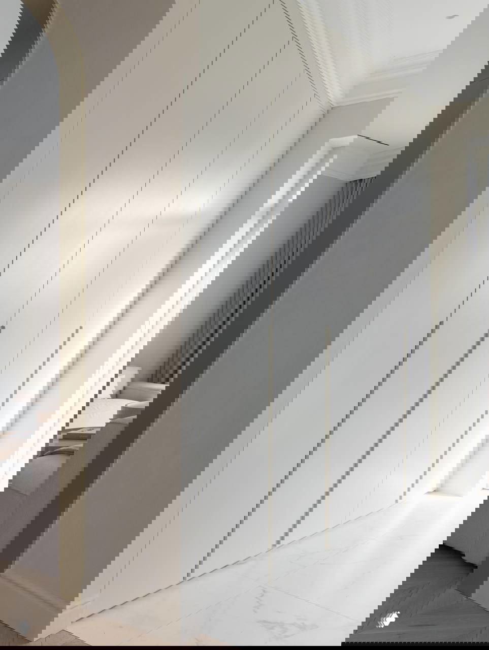 Встроенный шкаф в пастельных тонах с узкими вертикальными ручками на фоне светлого пола и арочного проема — пример продуманного хранения.