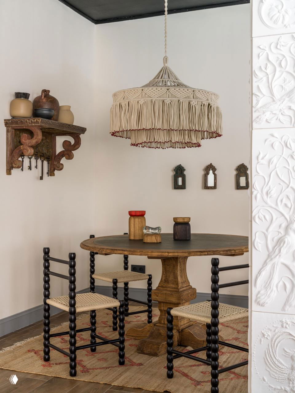 Обеденная зона с круглым деревянным столом, резными стульями и макраме‑люстрой над столом; на стене декоративные полочки с керамикой и ключами.