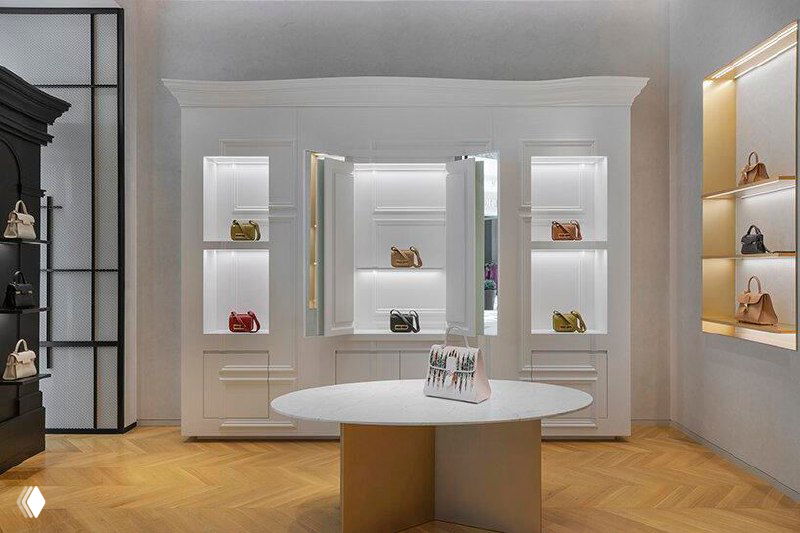 Вид на торговое пространство Delvaux: паркетный пол, плавные линии мебельных подиумов и строгая, но тёплая материальная фактура интерьера.