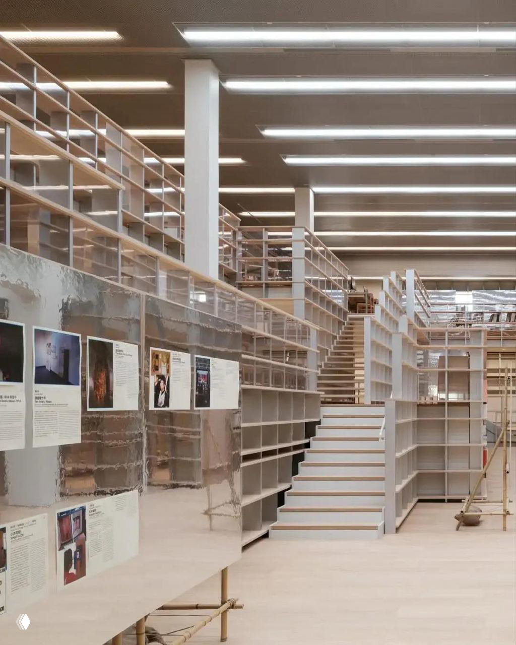 Часть библиотеки: зеркальные панели, пустые и частично заполненные стеллажи, лестница и организационные элементы пространства хранения книг.