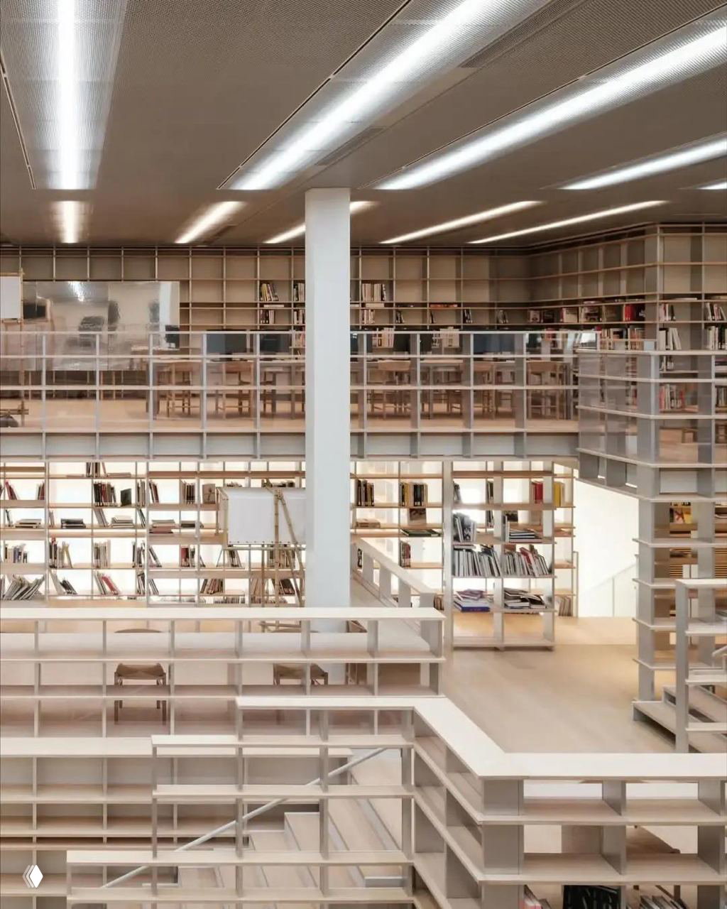 Многоярусные открытые стеллажи и галереи библиотеки с деревянными полками и распределением книг на разных уровнях в светлом интерьере.