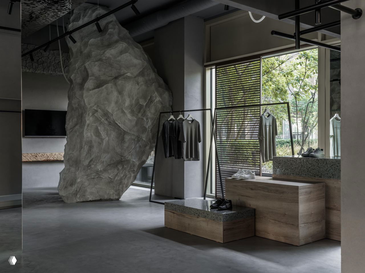 Драматичный каменный арт-объект и монохромная зона примерок на фоне мягкой серой отделки и текстурных поверхностей магазина