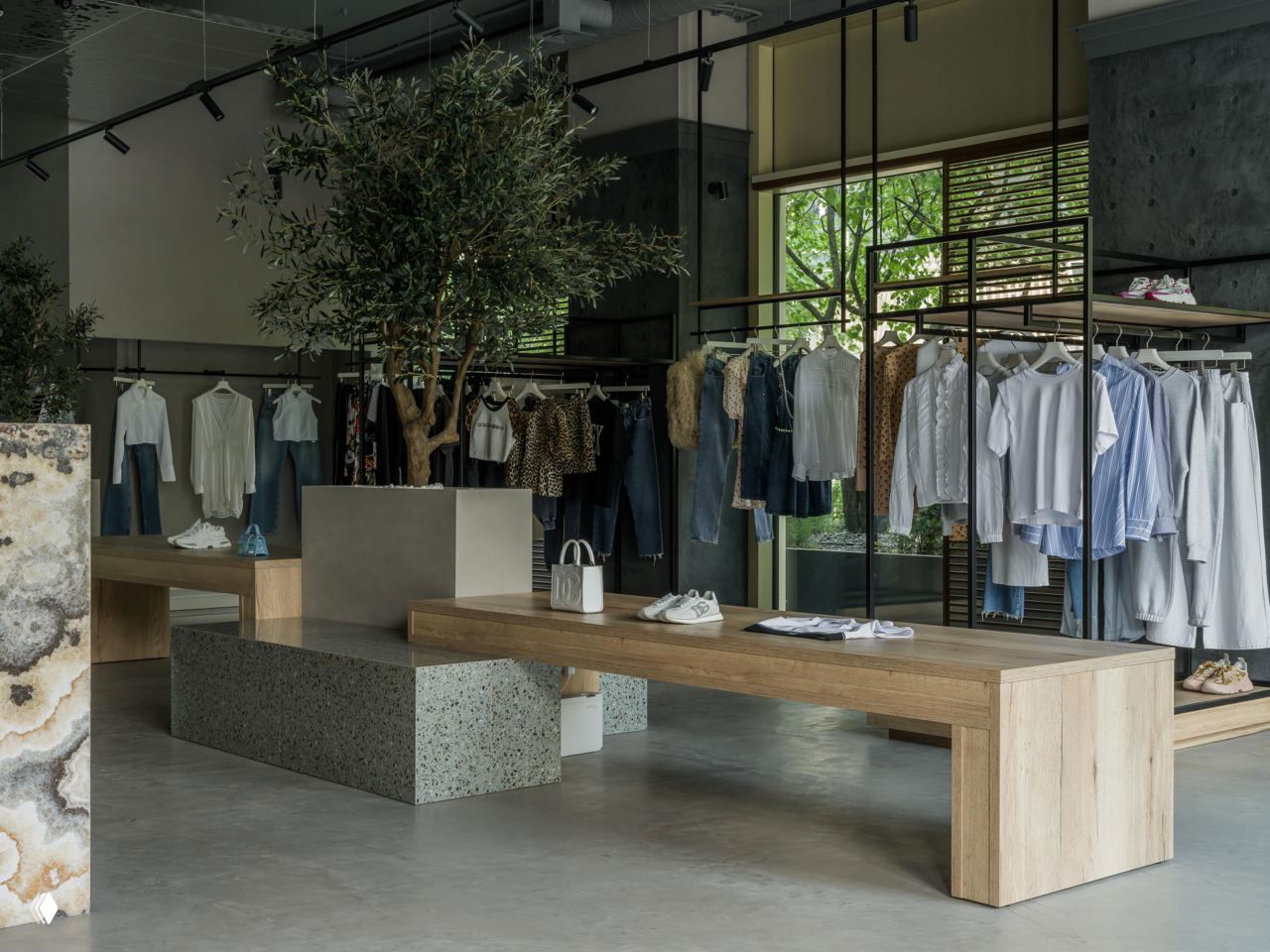 Витрина и показательная зона с лавками из светлого дерева и бетонными подиумами в бутике Ple Ple, одежда на минималистичных вешалах