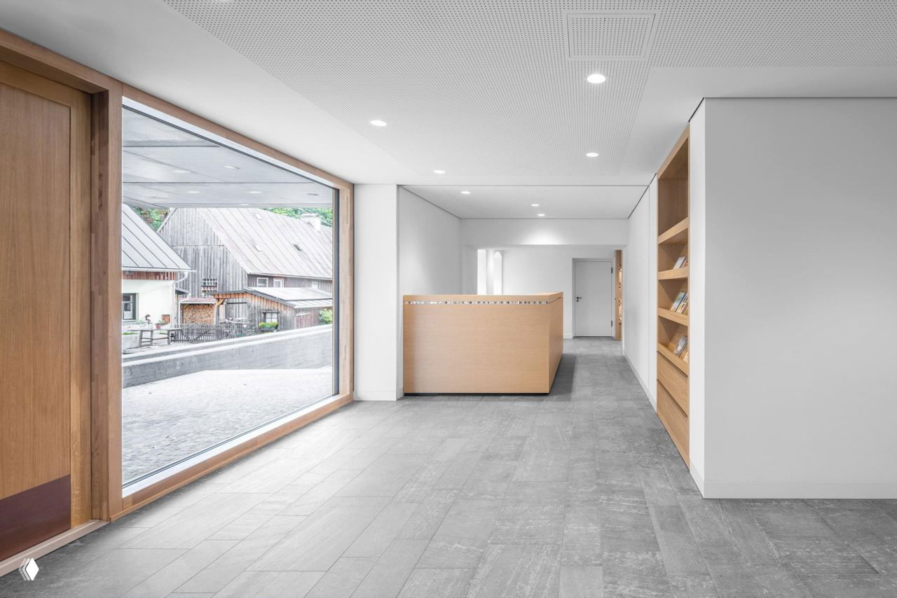 Интерьер фойе музея: белые гладкие поверхности, крупное окно с деревянной рамой и светлая приёмная зона с видом на старую часть города