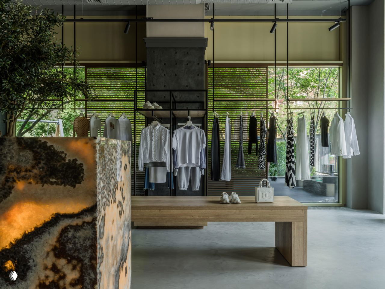 Широкий ракурс интерьера: ониксовая стойка, деревянные столы и крупные окна с видом на зелень во внешнем пространстве бутика