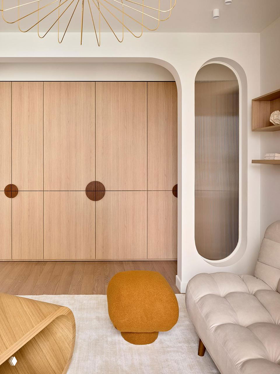 Узкий ракурс на встроенный шкаф из светлого дерева, арочные проемы и маленький терракотовый пуф на светлом ковре в общей зоне квартиры.