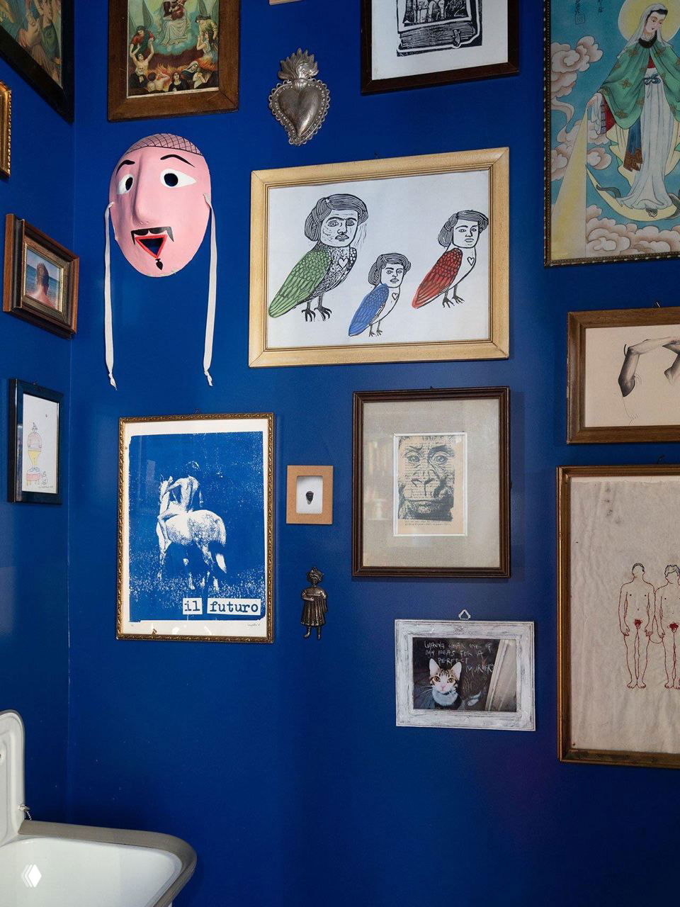 Насыщенная синяя стенa, собранная в галерее: маска, картины в рамах и различные декоративные элементы, яркий акцент в помещении.