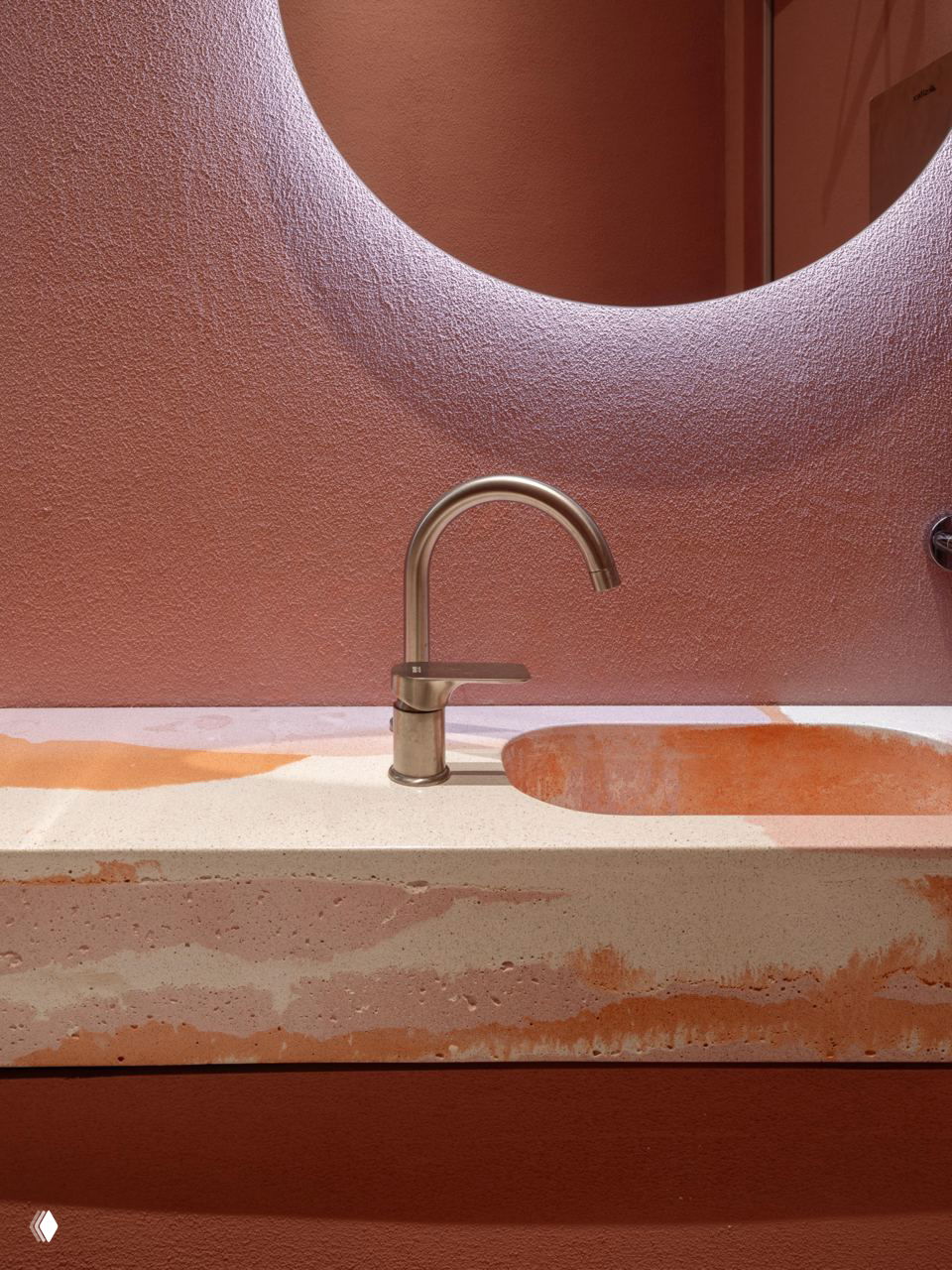 Деталь интерьера: раковина и столешница с пятнистой терракотовой текстурой на фоне розовой стены и круглого ниши с подсветкой.