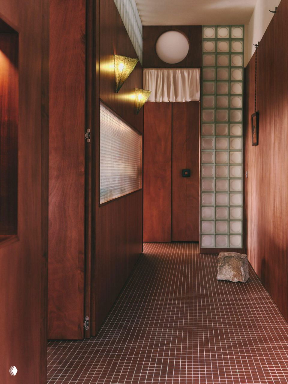 Длинный коридор студии с панелями из красного дерева и вертикальной колонной из стеклоблоков, мягкое рассеянное освещение.